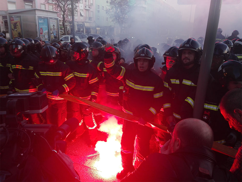 Protesting firefighters illuminated by red flare.